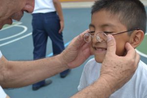 Fotografía de un paciente beneficiado por nuestro programa social ventanitas de luz mientras las manos de su padre le colocan bien los lentes a su hijo